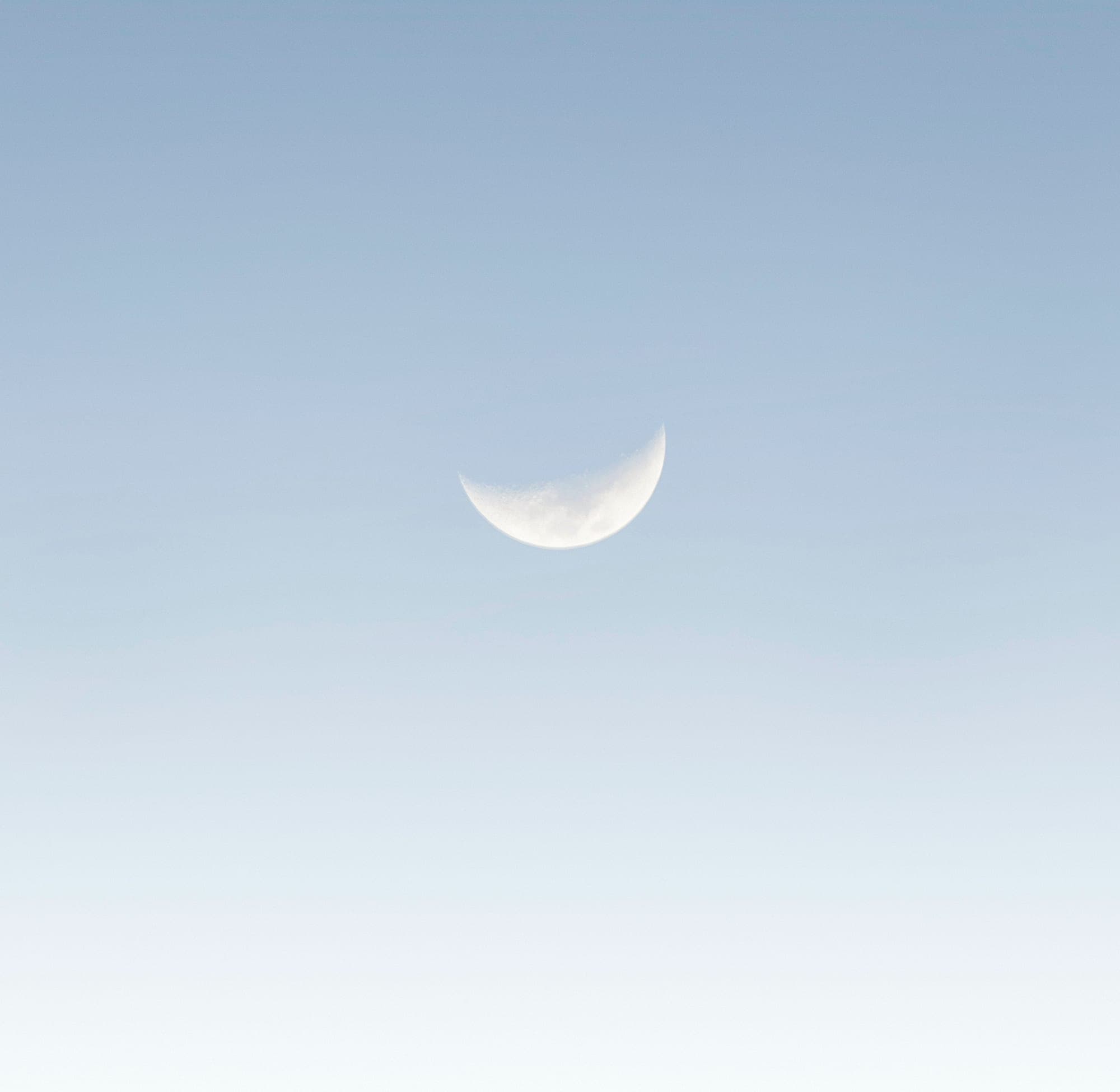 A waxing crescent moon high in a clear, pale blue sky.